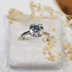 a diamond ring sitting on top of a white box next to flowers and dried grass