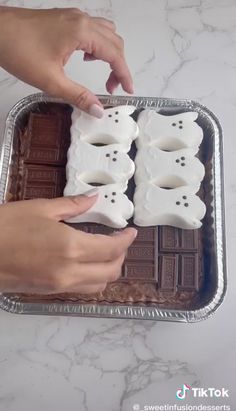 two hands reaching for some white chocolate in a pan on a marble counter top,