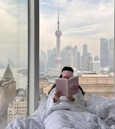 a woman laying in bed with a blind folded over her face and reading a book