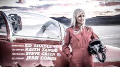 a woman in an orange jumpsuit standing next to a red plane with the pilot's helmet on