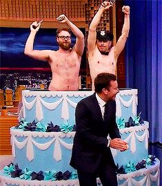 two men standing in front of a three tiered cake on the set of the tonight show