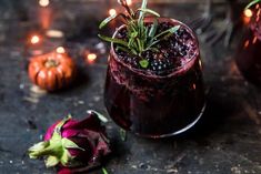 a glass filled with blackberries and topped with greenery next to some pumpkins