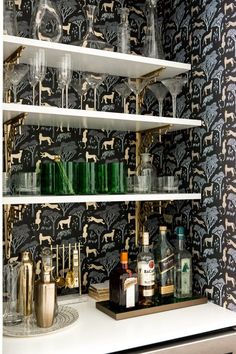 the shelves are filled with liquor bottles and glasses on top of each other in front of a wallpapered wall