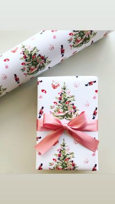 a present wrapped in wrapping paper with a pink bow on it next to a christmas tree