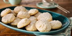 a blue bowl filled with sugar cookies on top of a wooden table next to a cup