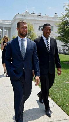 two men in suits walking down a sidewalk near the white house with one man wearing a suit and tie