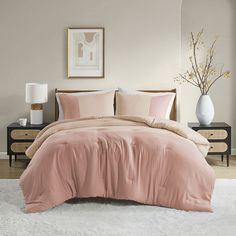 a bed with pink comforter and pillows in a white room next to a dresser