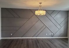 an empty room with wood flooring and gray painted walls, along with a chandelier