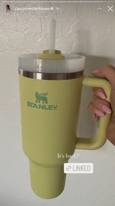 a person holding a yellow coffee cup with a straw in it's mouth and the word stanley on the side