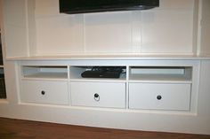 a flat screen tv mounted to the side of a white entertainment center with drawers underneath it