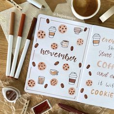 an open notebook with coffee and cookies on it next to some markers, pens and pencils