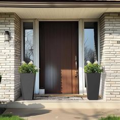 two large planters with flowers are in front of a brown door on a brick house