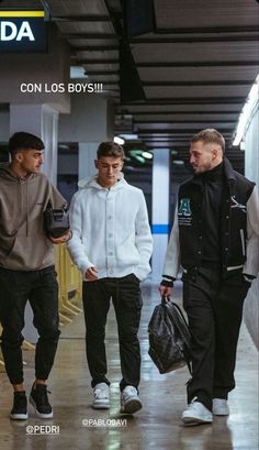 three young men are walking through an airport terminal, one is carrying a black bag