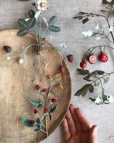 a wooden plate with flowers and berries on it, being held by someone's hand