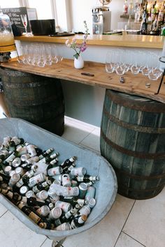 This shows a bar area at a barn wedding. This focuses on a barrel bar display, which are two large barrels with a wooden board over it. On the board are some glasses and drink dispensers. In front of the barrel is a large galvanised bath with beers in it. Wedding Bar Area, Bar Hire