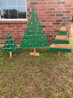 three wooden christmas trees sitting in front of a brick building with grass on the ground