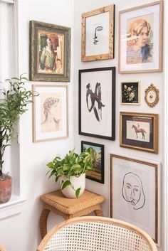 there are many framed pictures on the wall next to a table with a potted plant