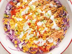 a colorful salad with chicken, corn and dressing in a white bowl on top of a wooden table