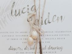 the wedding stationery is adorned with pearls and twine to hang on a palm tree branch