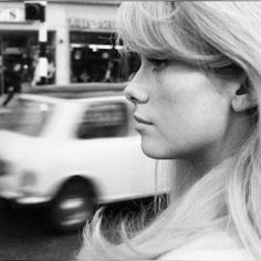 a black and white photo of a woman on the street with cars in the background