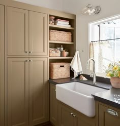 a kitchen sink sitting under a window next to a counter top with baskets on it