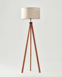 a wooden tripod floor lamp with a linen shade on it's top and bottom