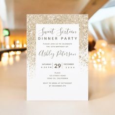 a white and gold glitter dinner party card on a table with candles in the background