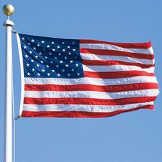 an american flag flying in the wind with a blue sky behind it and a gold ball on top