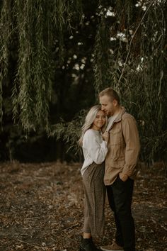 an engaged couple standing under a tree in the woods