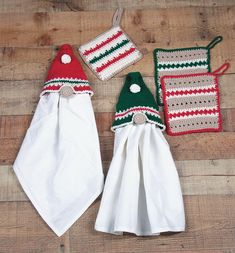 three kitchen towels and two crocheted santa hats on a wooden table with white cloths