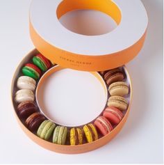 an assortment of colorful macaroons are in a cardboard box on a white surface