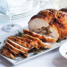 a white plate topped with sliced turkey next to wine glasses and plates filled with food