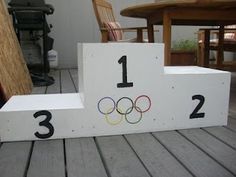 a wooden box with the olympic rings on it sitting on a deck next to a table