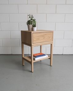 a small wooden table with a plant on top and books under it, against a white brick wall