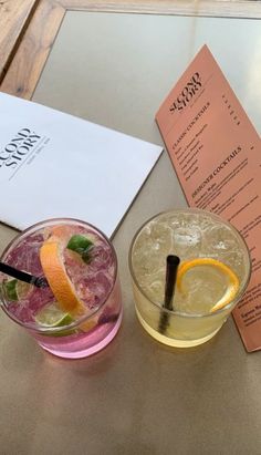 two cocktails sitting on top of a table next to an orange slice and menu