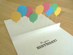 a birthday card with balloons sticking out of the inside of it on top of a table