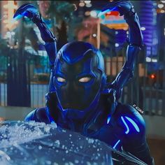 a man dressed as a blue beetle with his hands in the air