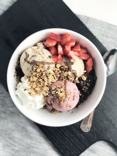 a bowl filled with ice cream, strawberries and granola on top of a table