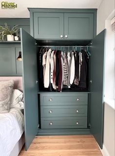 an open closet with clothes hanging on hooks and drawers in front of a bed, next to a wooden floor