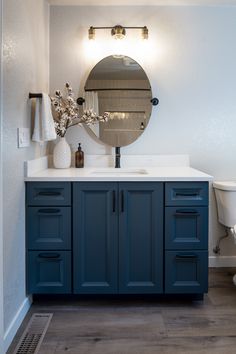 a white toilet sitting next to a bathroom sink under a mirror on top of a wooden cabinet