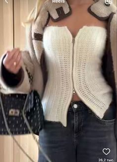 a woman in jeans and a white sweater holding a cell phone up to her chest