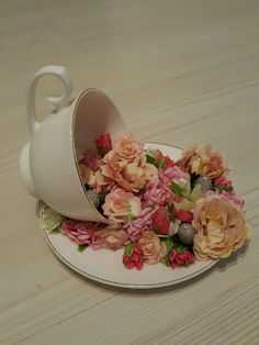 a white tea cup with pink and yellow flowers on it sitting on top of a plate