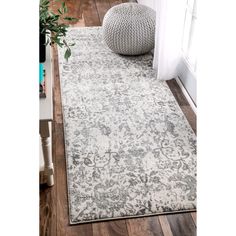 a white and gray rug on a wooden floor next to a window with a plant in the corner