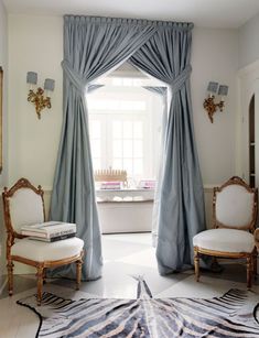 a living room with two chairs and a rug in front of a window that has blue drapes on it