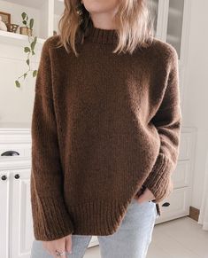 a woman wearing a brown sweater standing in front of a white cabinet and looking off to the side