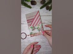 two hands are holding a small card and some pine cones on a white wooden table