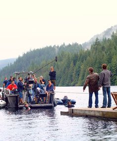 a group of people standing on top of a pier next to a body of water