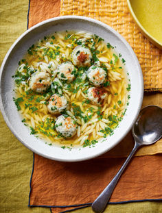 a bowl filled with pasta and meatballs on top of a yellow place mat next to a spoon