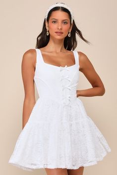 An awe-inspiring look like the Rare London Truly Flawless White Lace Sleeveless Bow Bustier Mini Dress deserves to be shown off and admired! This seriously romantic lace dress starts with wide straps, a square neckline, and a bustier-style bodice with supportive boning throughout and a row of dainty bows that run along the center. The fitted waist tops a tiered, skater-style skirt (with a hidden layer of organza for volume) that ends at a flirty mini hem. Hidden back zipper/clasp. Fit: This garm Chic Sleeveless Corset With Lace-up Back, Flirty Lace Mini Dress With Lace Bodice, Summer Wedding Mini Dress With Lace Bodice, Feminine Sleeveless Mini Dress With Delicate Lace, Summer Lace Dress With Corset Back, Square Neck Lace Dress With Lace Patchwork, Feminine Lace Mini Dress With Lace-up Back, Flirty Sleeveless Lace Dress With Lace Trim, Flirty Lace Dress With Sweetheart Neckline