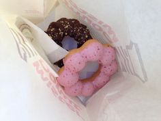 there are three donuts in the paper bag on the table and one is pink with sprinkles